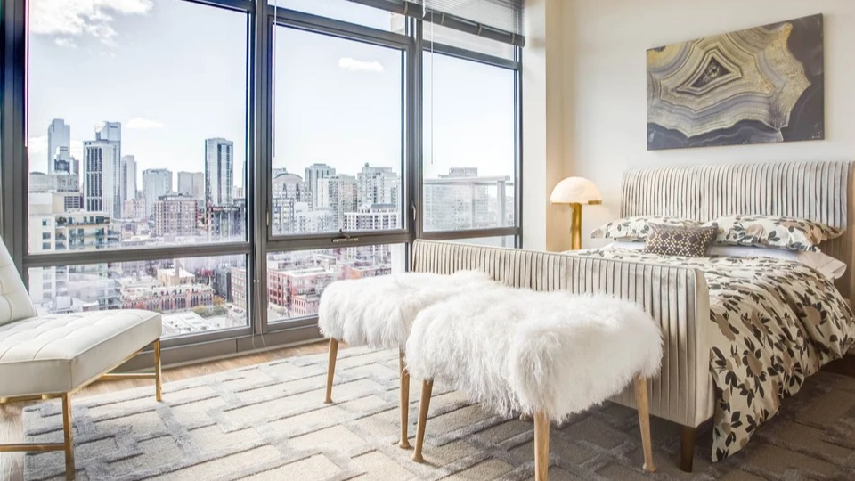 Cozy bedroom with a plush bed, floor-to-ceiling windows, and stunning city views at NEXT Apartments in Chicago