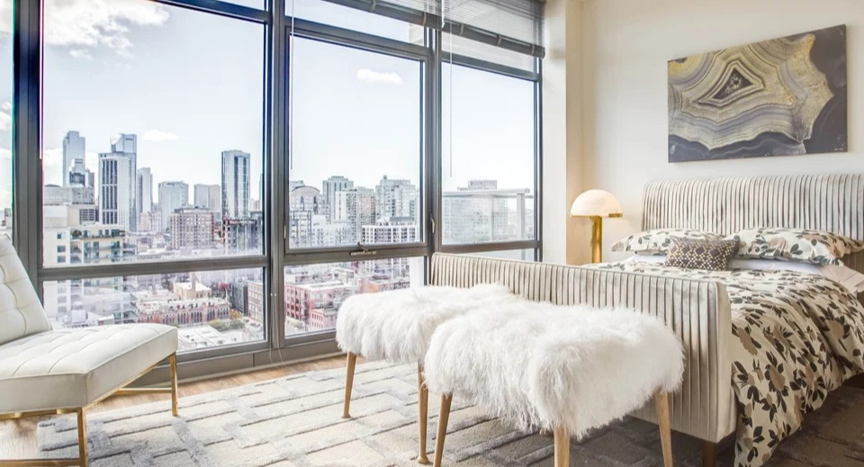 Cozy bedroom with a plush bed, floor-to-ceiling windows, and stunning city views at NEXT Apartments in Chicago