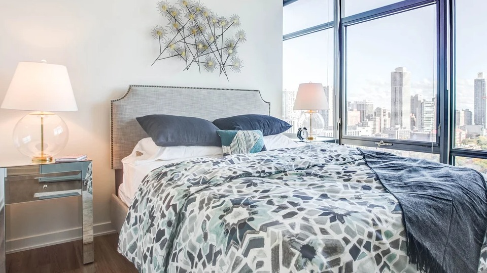 Elegant bedroom with a comfortable bed, chic decor, and expansive cityscape views at NEXT Apartments in Chicago