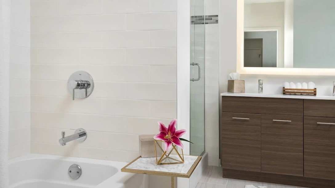 Modern bathroom with a clean design, white tile bathtub, glass shower, and illuminated mirror at NEXT Apartments in Chicago