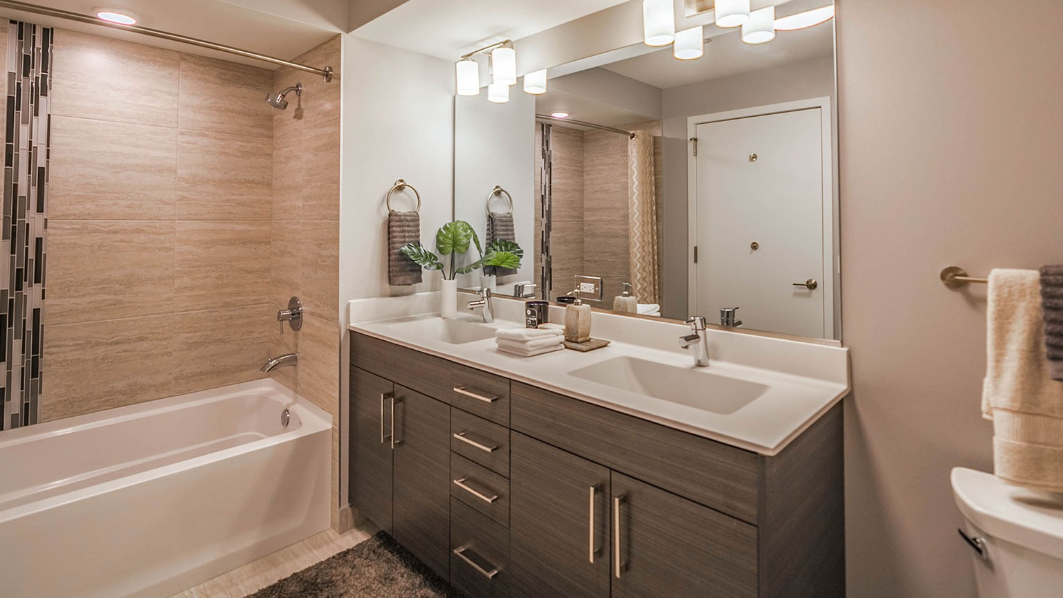 Modern apartment bathroom at Niche 905 in Chicago, featuring a double vanity, large mirror, and a bathtub with a shower