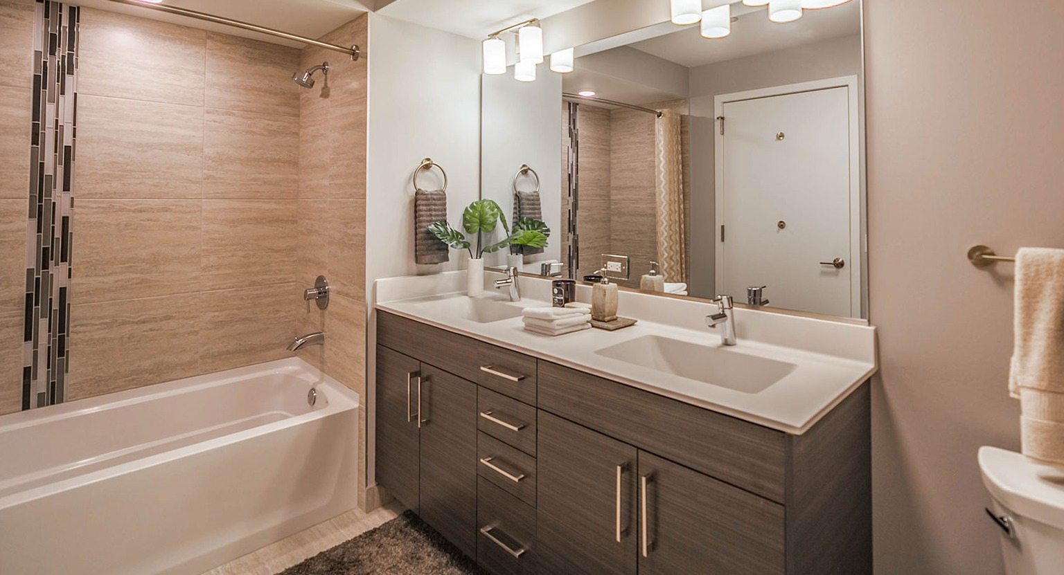 Modern apartment bathroom at Niche 905 in Chicago, featuring a double vanity, large mirror, and a bathtub with a shower