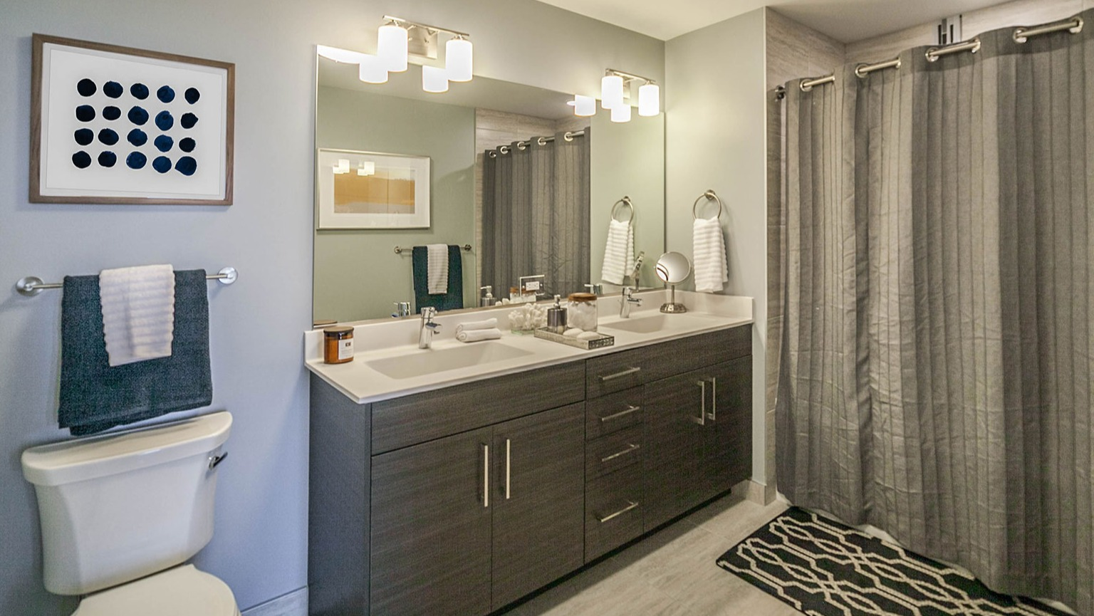 Modern apartment bathroom at Niche 905 in Chicago, featuring a double vanity, toilet, and a large walk-in shower with sleek tiles