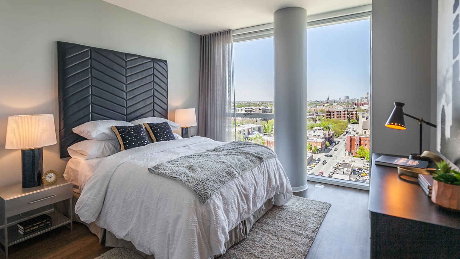 Modern bedroom at Niche 905 in Chicago, featuring a stylish headboard, comfortable bed, and large windows with city street views
