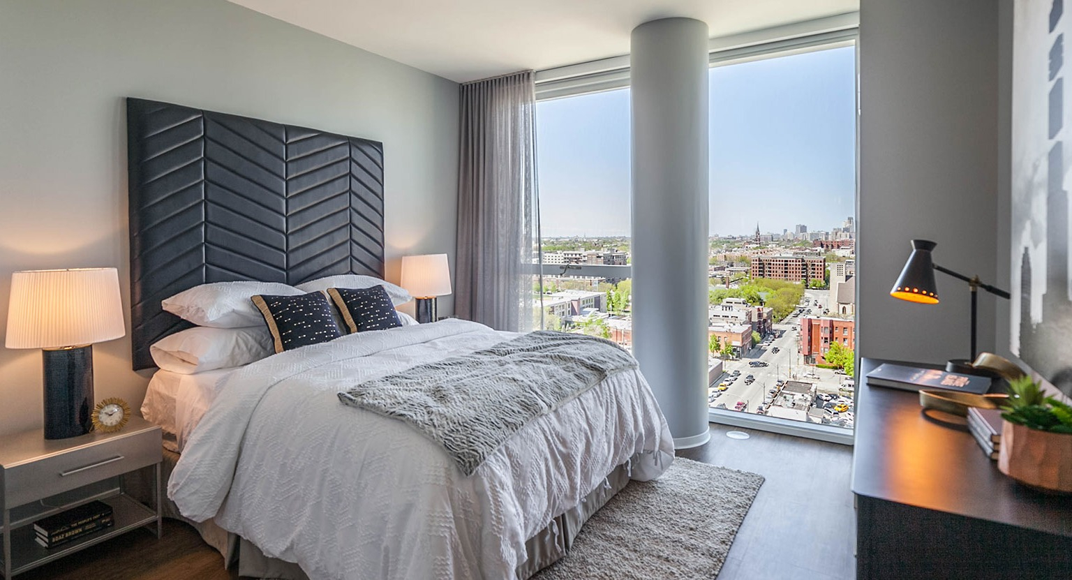 Modern bedroom at Niche 905 in Chicago, featuring a stylish headboard, comfortable bed, and large windows with city street views