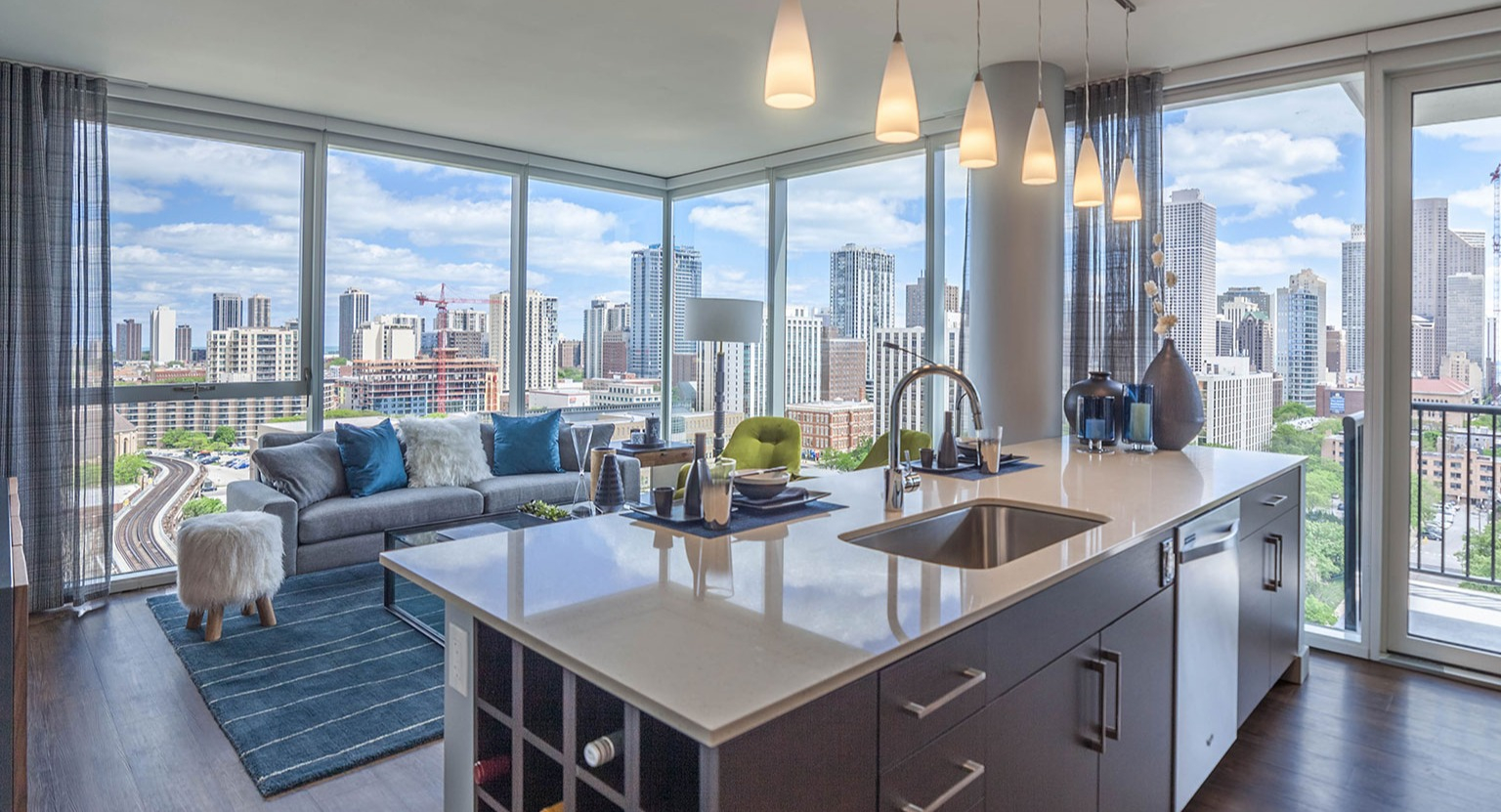 Bright apartment living room at Niche 905 in Chicago, featuring a modern kitchen island, comfortable sofa, and panoramic city views