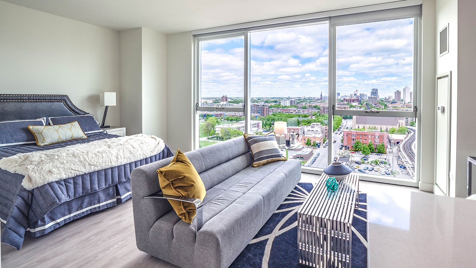 Chic studio apartment at Niche 905 in Chicago, featuring a stylish bed, modern sofa, and expansive city views through large windows