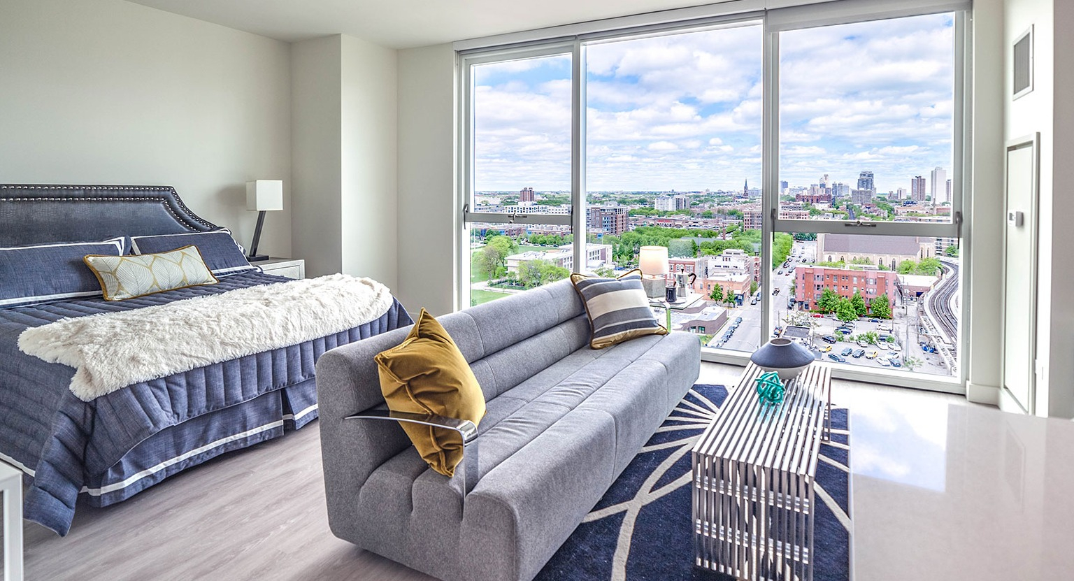 Chic studio apartment at Niche 905 in Chicago, featuring a stylish bed, modern sofa, and expansive city views through large windows