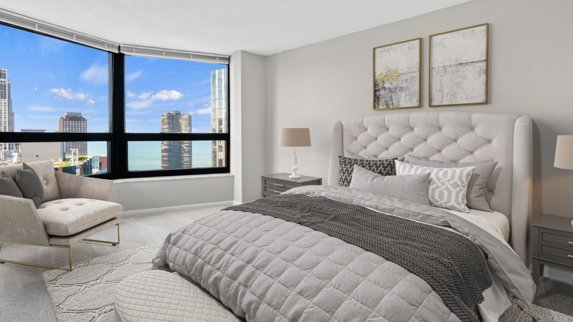Sunlit bedroom corner with an upholstered bed, wall-mounted sconces, modern artwork, and large windows showcasing downtown city views at North Harbor Tower in Chicago