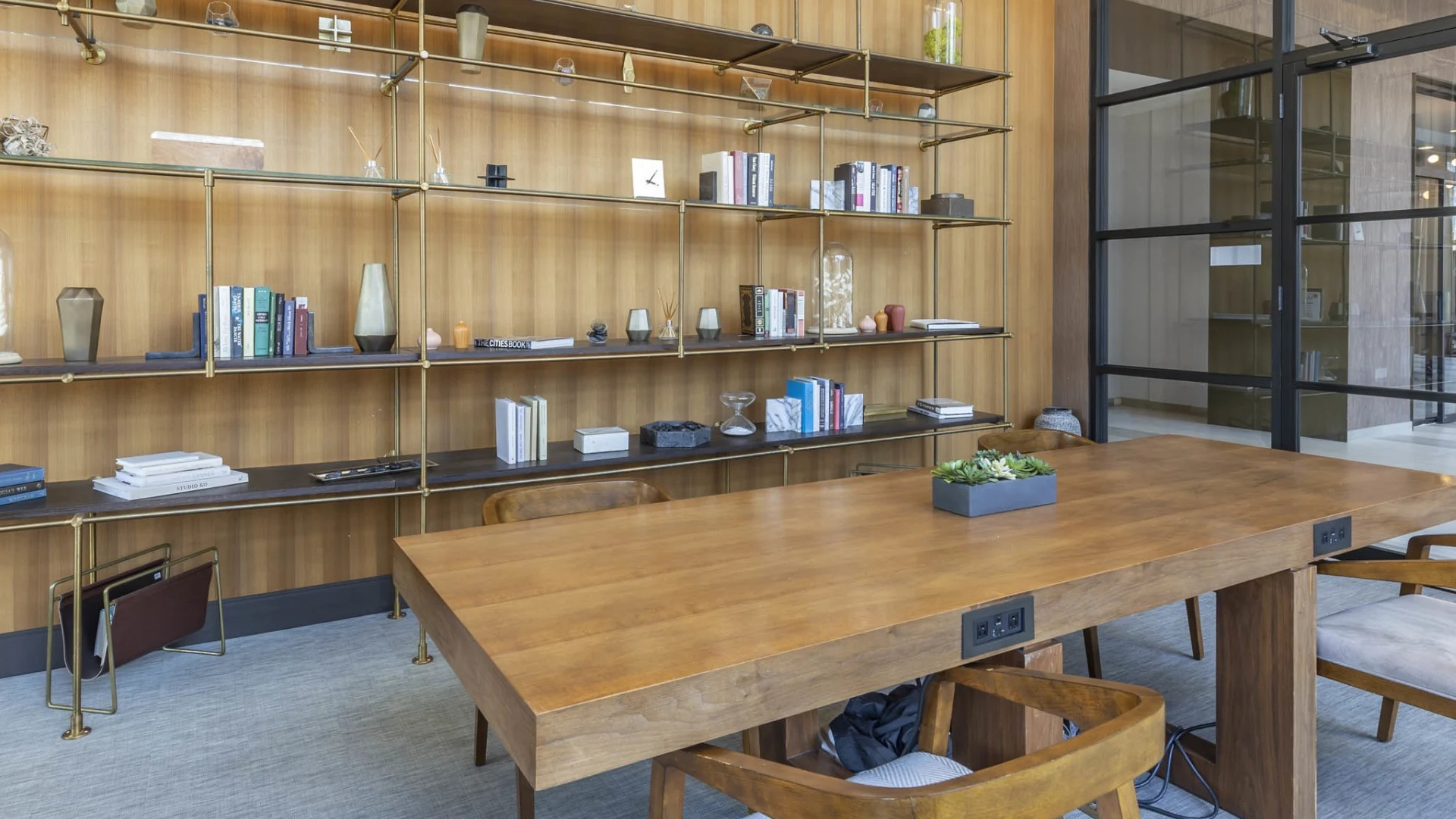 Stylish coworking library at North Harbor Tower in Chicago with built-in brass shelving, wood table, modern lighting, and glass doors—ideal for studying or remote work