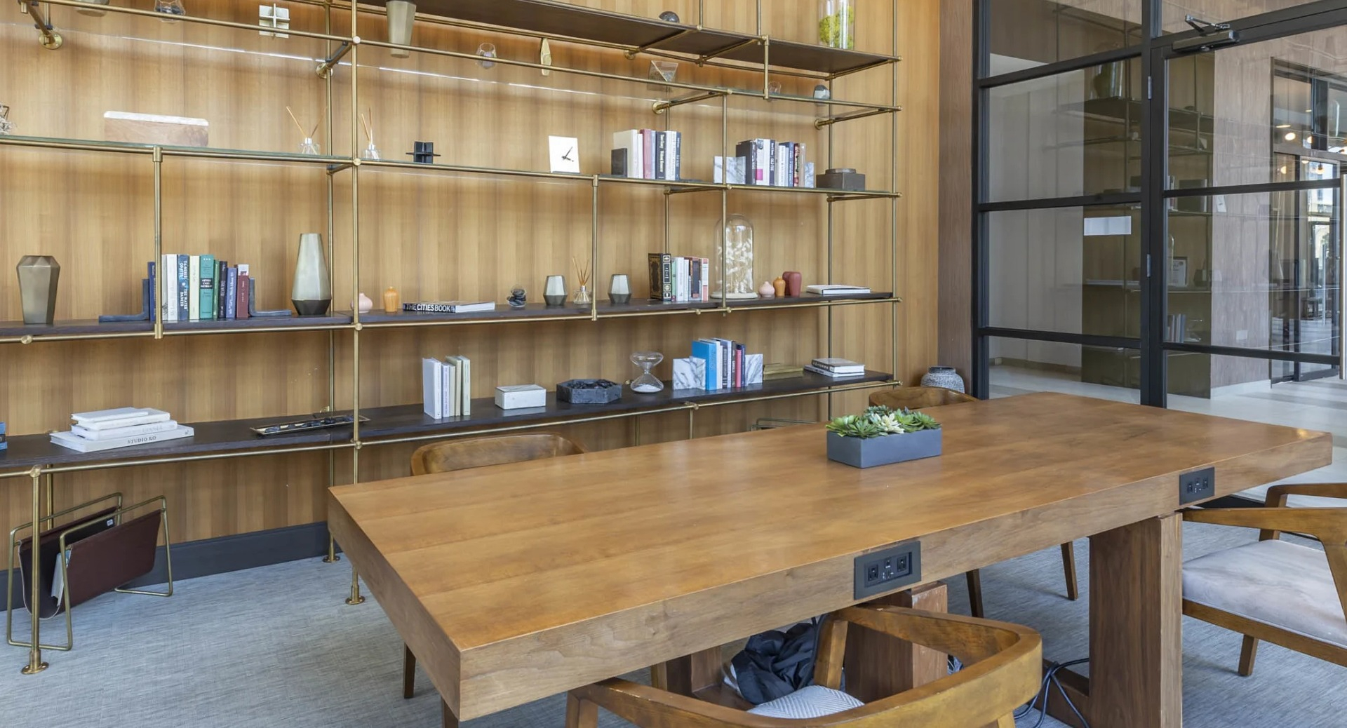 Stylish coworking library at North Harbor Tower in Chicago with built-in brass shelving, wood table, modern lighting, and glass doors—ideal for studying or remote work