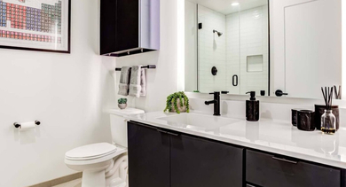 Modern bathroom with a black vanity, white counter, glass shower, and a minimalist design at North+Vine in Chicago