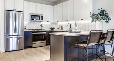 Modern kitchen featuring a large island with bar seating, white upper cabinets, dark lower cabinets, and stainless steel appliances at North+Vine in Chicago