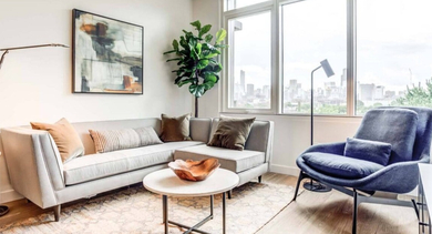 Stylish living room with a grey sectional, cozy armchair, and large corner windows offering expansive city views at North+Vine in Chicago