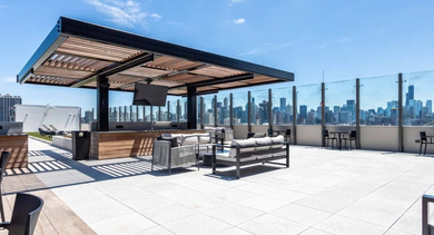 Modern rooftop outdoor kitchen and lounge area with covered seating, grills, and panoramic city views at North+Vine in Chicago