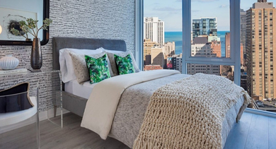 Chic bedroom with textured wallpaper, a comfortable bed, and floor-to-ceiling windows showcasing lake and city skyline views at OLD TOWN PARK ONE in Chicago