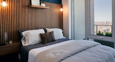 Stylish bedroom with a dark blue accent wall, slatted wood headboard, ambient lighting, and large windows at OLD TOWN PARK THREE in Chicago