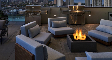 Luxurious rooftop terrace at dusk with a cozy fire pit, comfortable lounge seating, and grilling stations with city views at OLD TOWN PARK THREE in Chicago