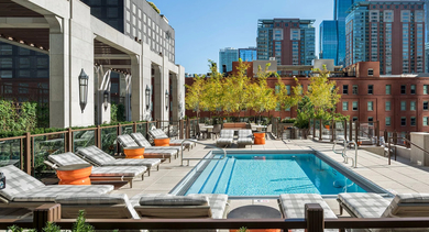 Luxurious outdoor pool deck at One Bennett Park Apartments in Chicago, featuring lounge chairs, lush greenery, and city views