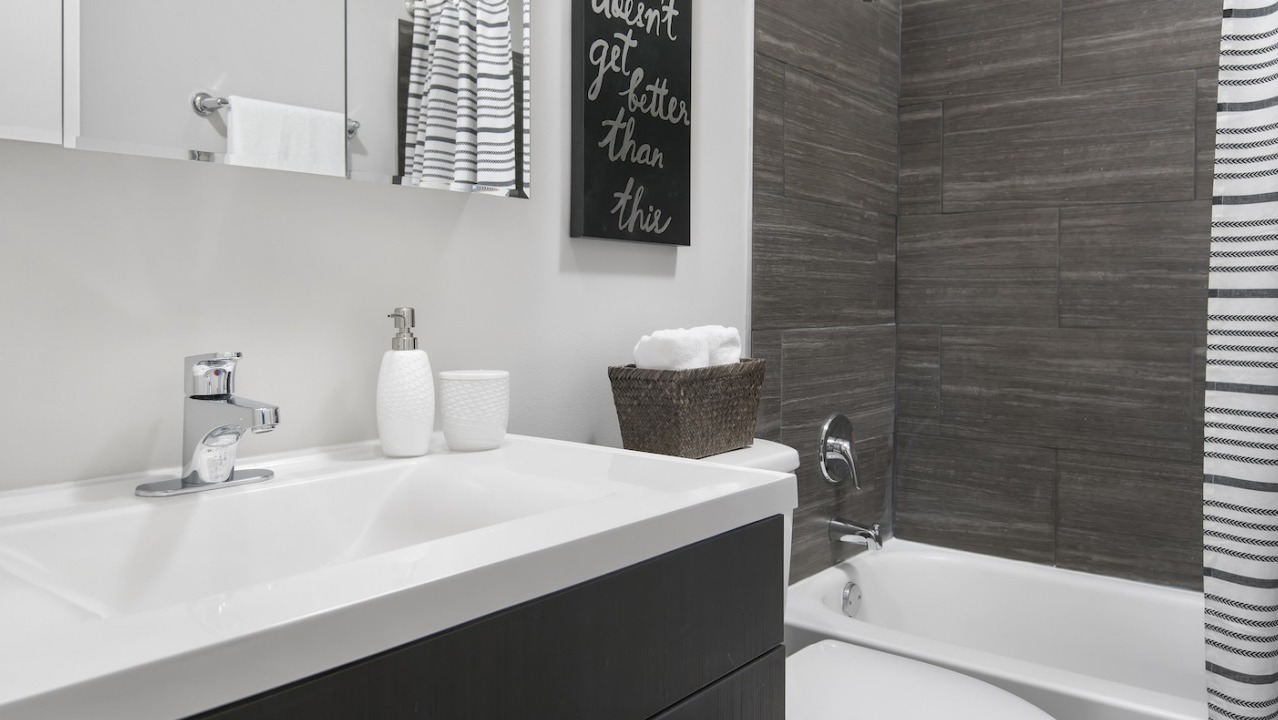 Contemporary bathroom with a modern vanity, dark tiled shower, and striped shower curtain at One East Delaware Apartments