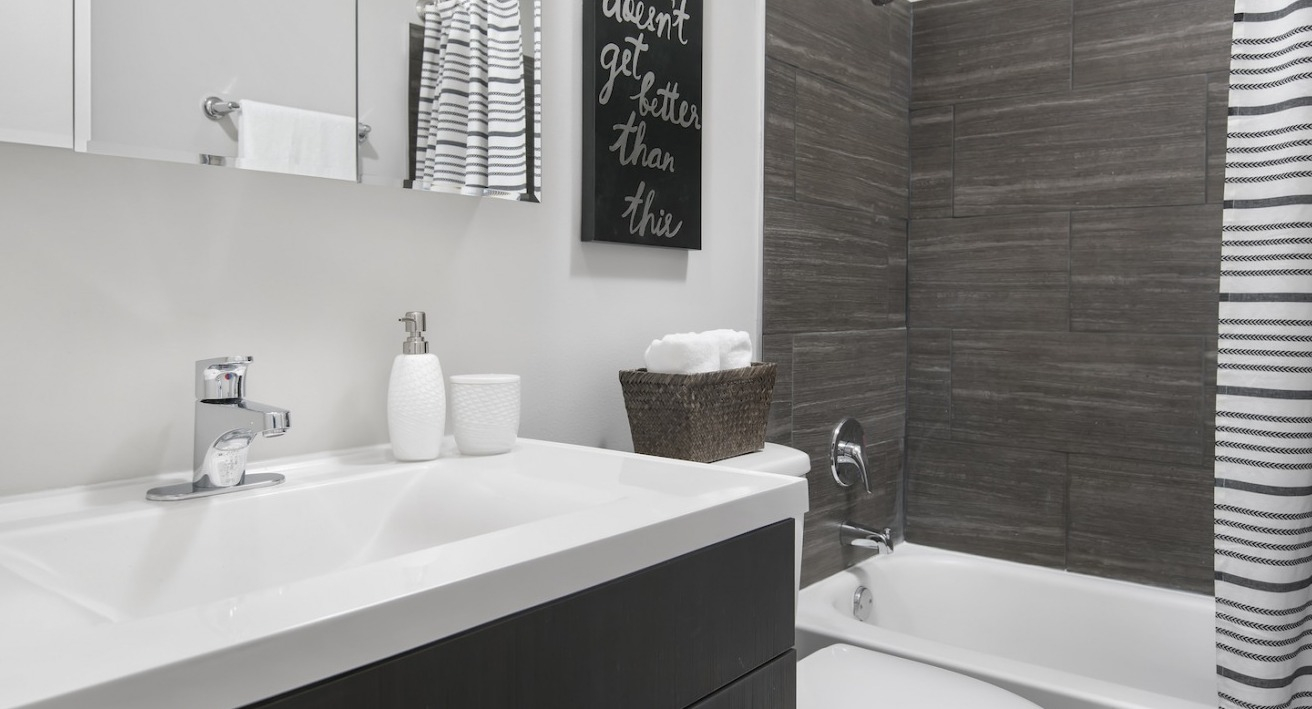 Contemporary bathroom with a modern vanity, dark tiled shower, and striped shower curtain at One East Delaware Apartments