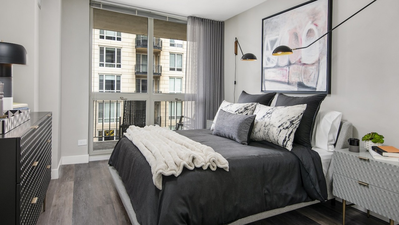 Cozy and modern bedroom with dark bedding, chic lighting, and a large window, offering a peaceful retreat at One East Delaware Apartments