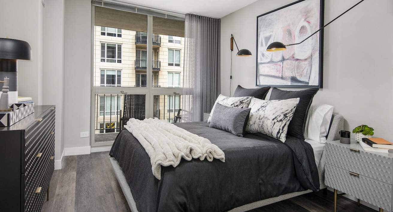 Cozy and modern bedroom with dark bedding, chic lighting, and a large window, offering a peaceful retreat at One East Delaware Apartments