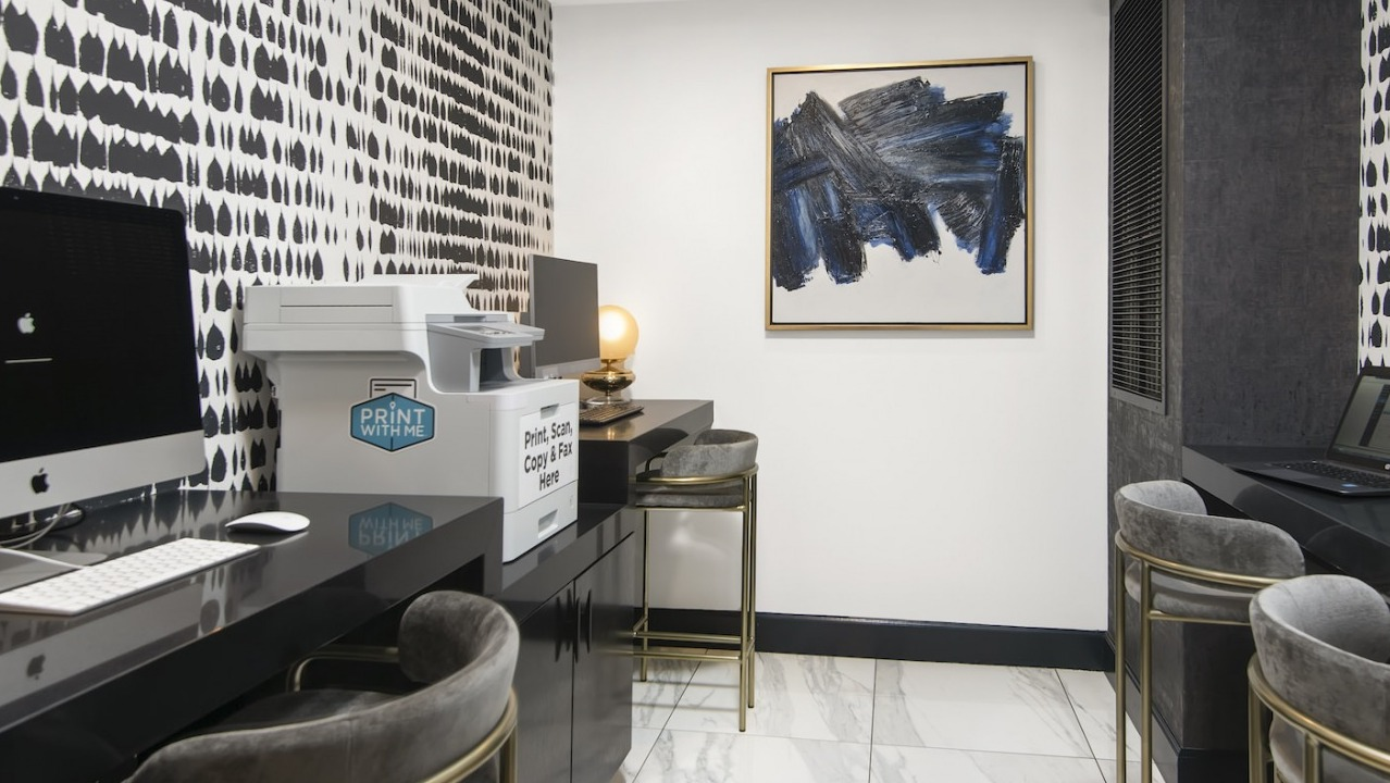 Modern business center with multiple workstations, computers, a printer, and stylish decor at One East Delaware Apartments