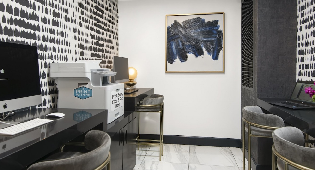 Modern business center with multiple workstations, computers, a printer, and stylish decor at One East Delaware Apartments