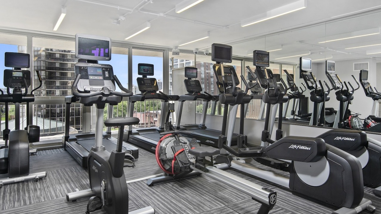 Modern cardio gym with treadmills, ellipticals, rowing machines, and large windows offering city views at One East Delaware Apartments