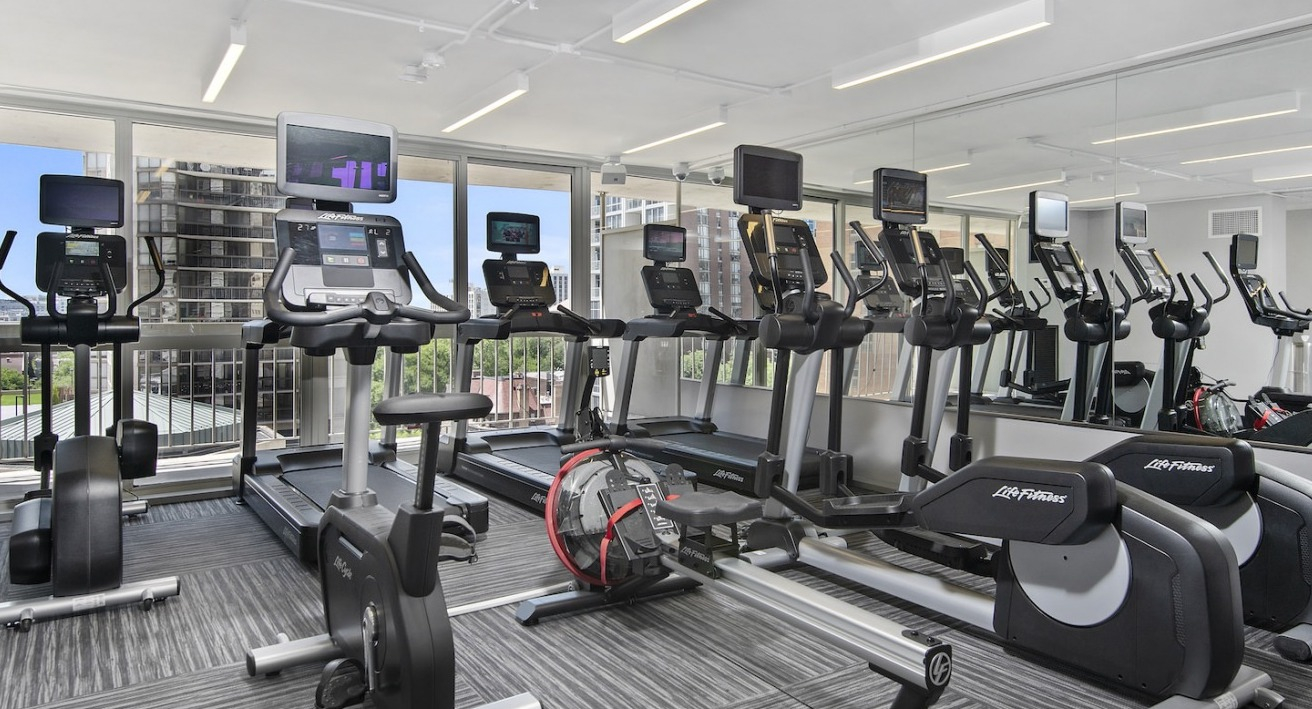 Modern cardio gym with treadmills, ellipticals, rowing machines, and large windows offering city views at One East Delaware Apartments
