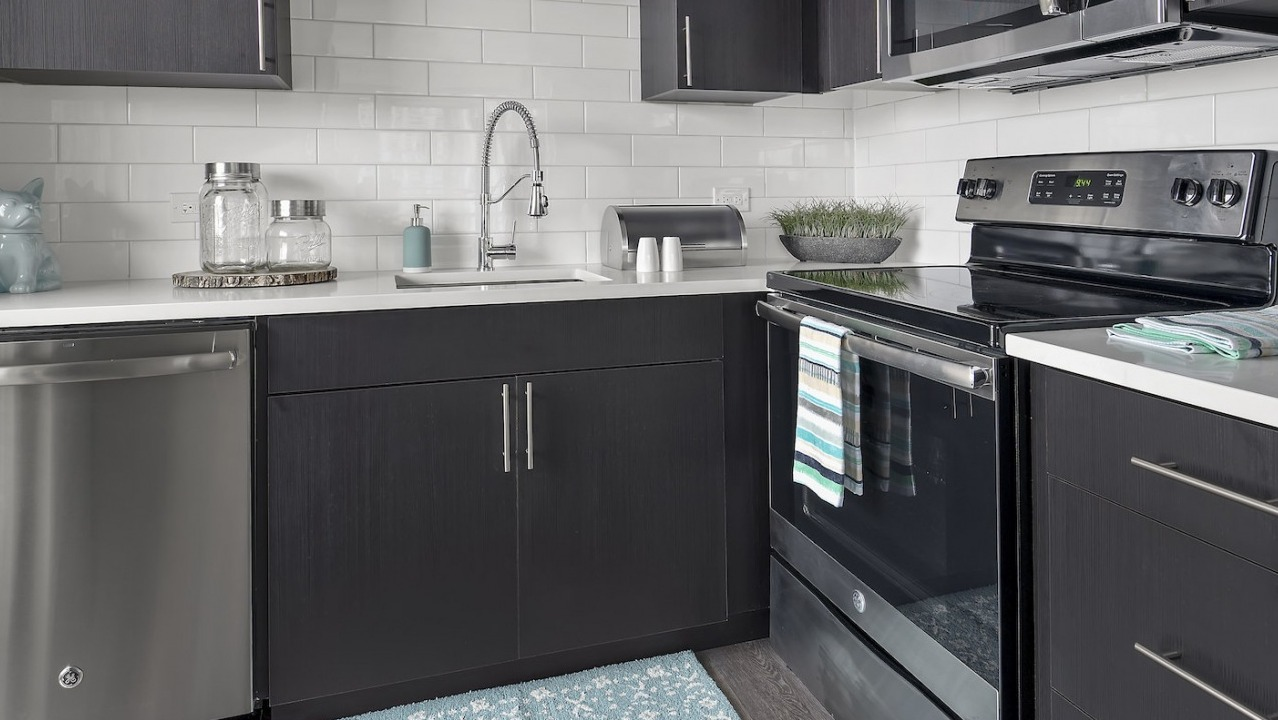 Modern kitchen with dark cabinetry, white subway tile backsplash, and stainless steel appliances at One East Delaware Apartments