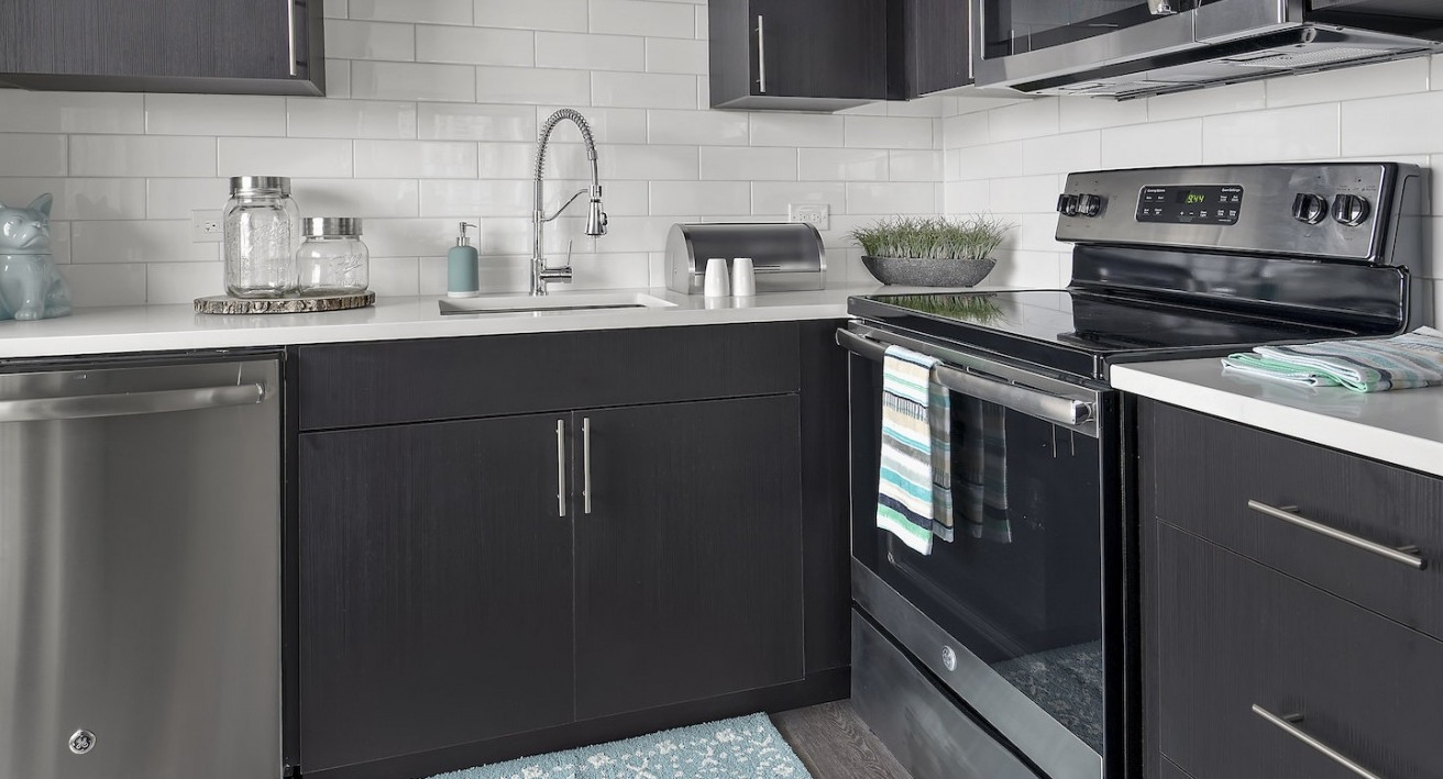 Modern kitchen with dark cabinetry, white subway tile backsplash, and stainless steel appliances at One East Delaware Apartments
