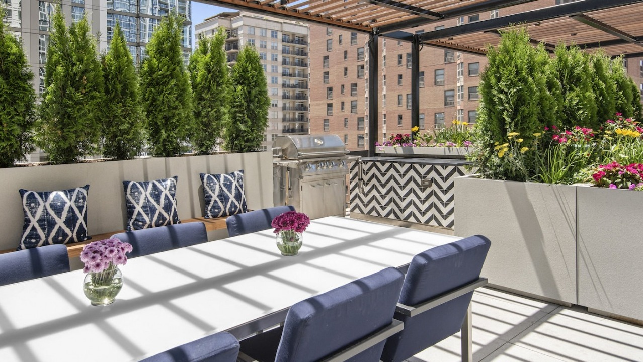 Elegant rooftop dining area with a long table, comfortable seating, grilling stations, and lush greenery at One East Delaware Apartments