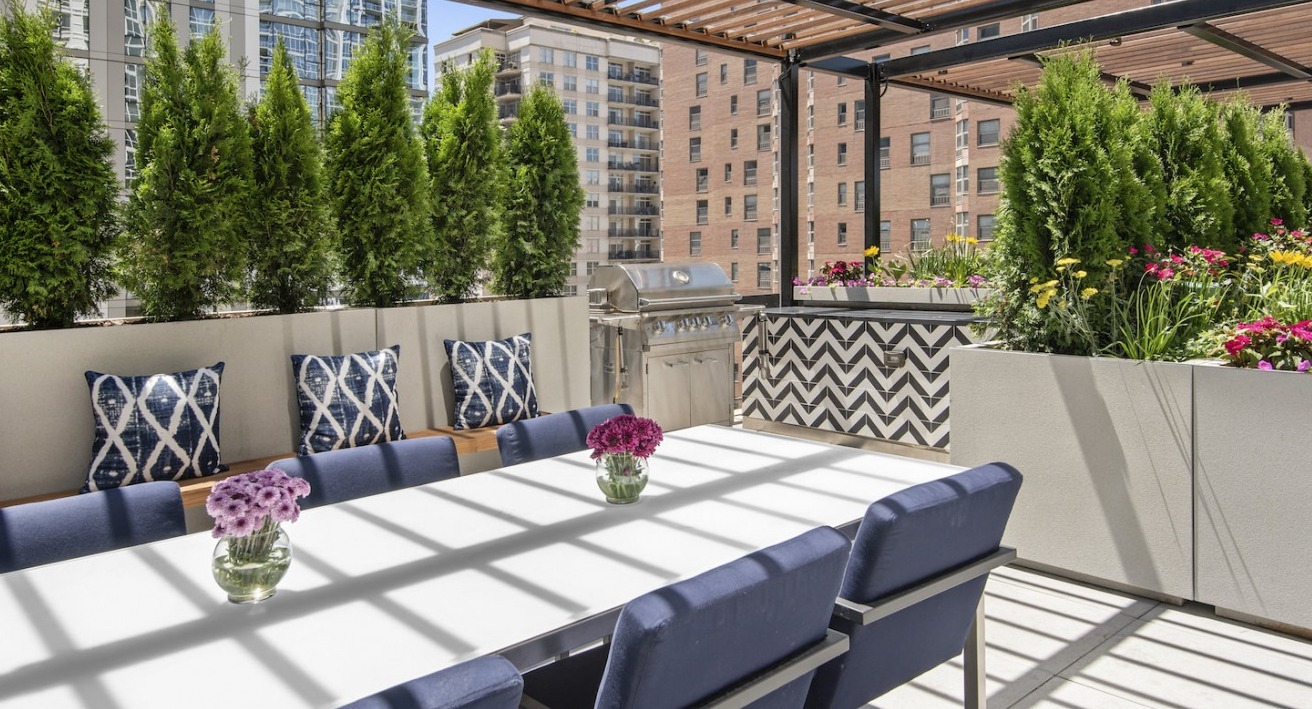 Elegant rooftop dining area with a long table, comfortable seating, grilling stations, and lush greenery at One East Delaware Apartments