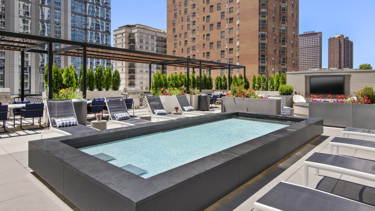 Sunlit rooftop pool area with comfortable lounge chairs, outdoor TV, and beautiful city views at One East Delaware Apartments