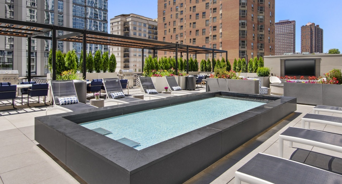 Sunlit rooftop pool area with comfortable lounge chairs, outdoor TV, and beautiful city views at One East Delaware Apartments
