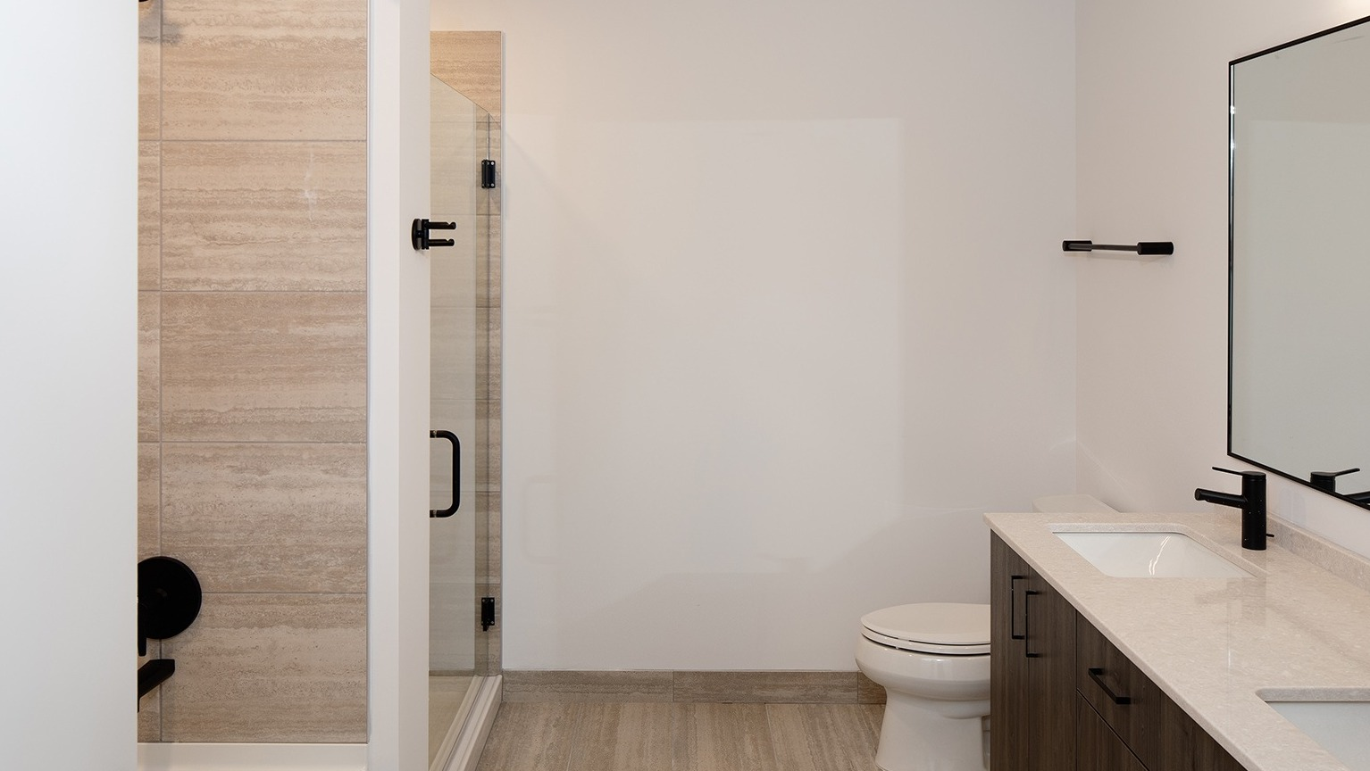 Spacious bathroom with a double vanity, dark wood-look cabinetry, and a glass-enclosed shower at One Six Six