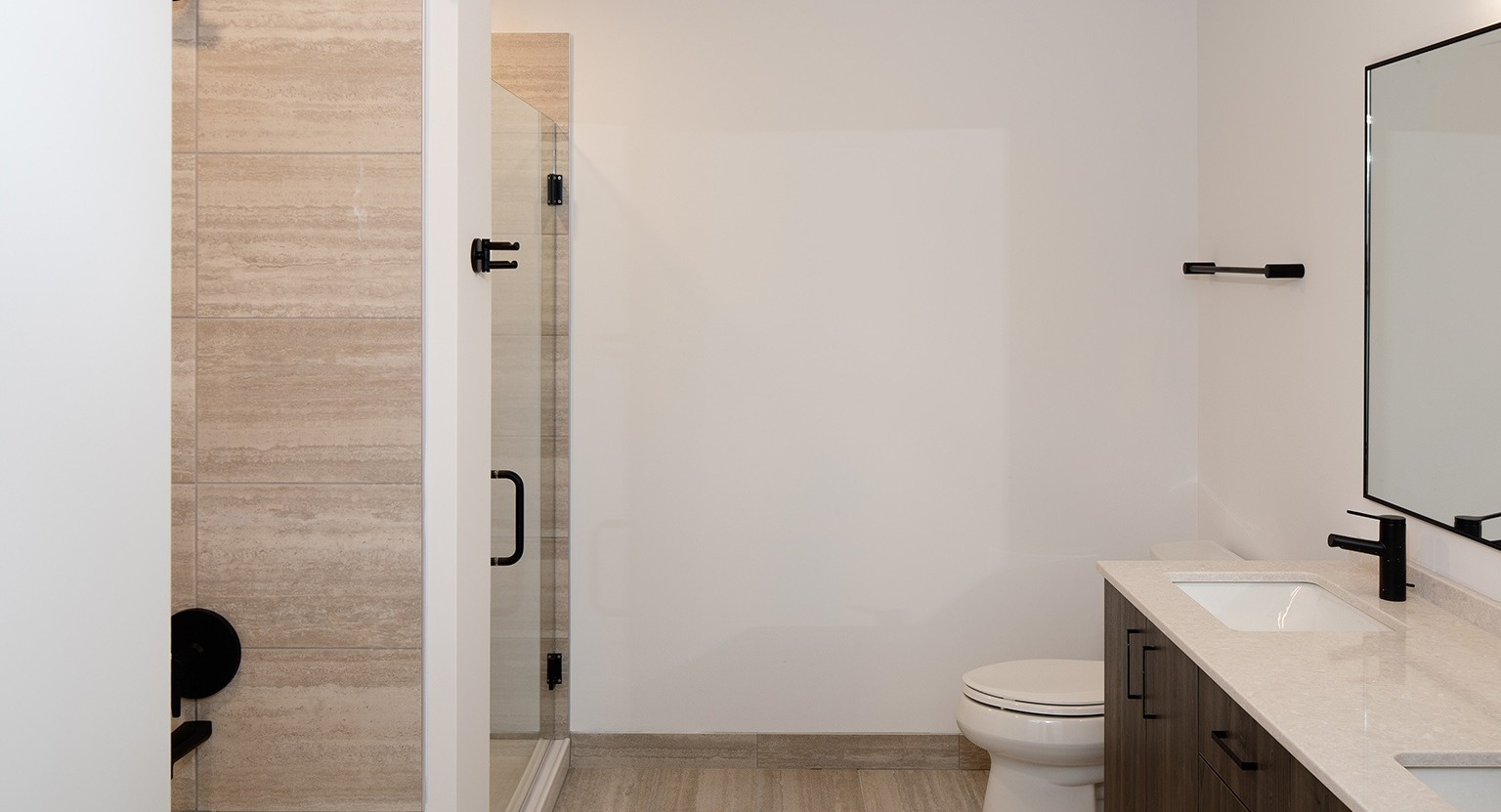 Spacious bathroom with a double vanity, dark wood-look cabinetry, and a glass-enclosed shower at One Six Six