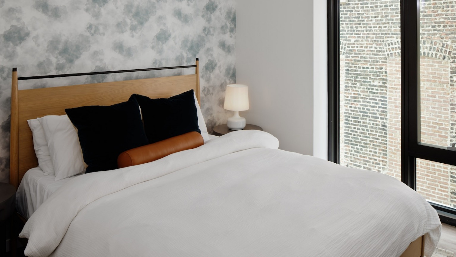 Cozy bedroom with a comfortable bed, stylish patterned wallpaper, and a large window offering natural light at One Six Six