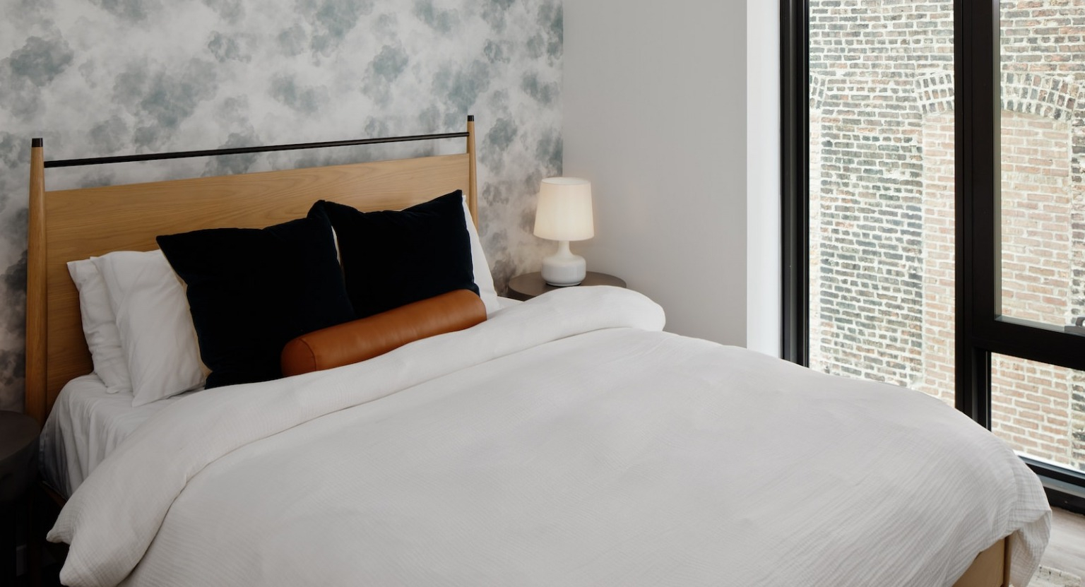 Cozy bedroom with a comfortable bed, stylish patterned wallpaper, and a large window offering natural light at One Six Six