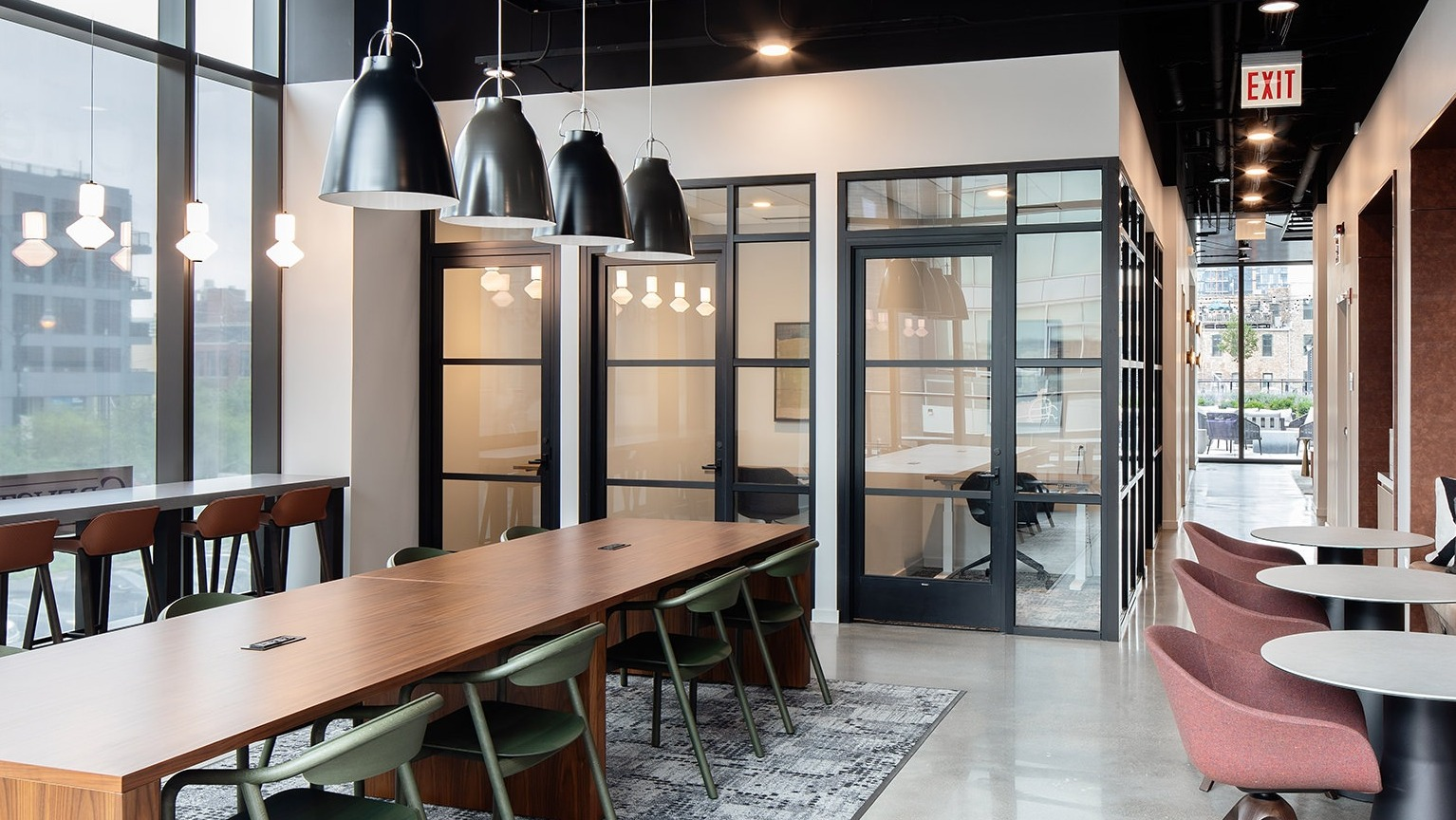 Modern coworking space with a large communal table, private offices, and comfortable booth seating at One Six Six