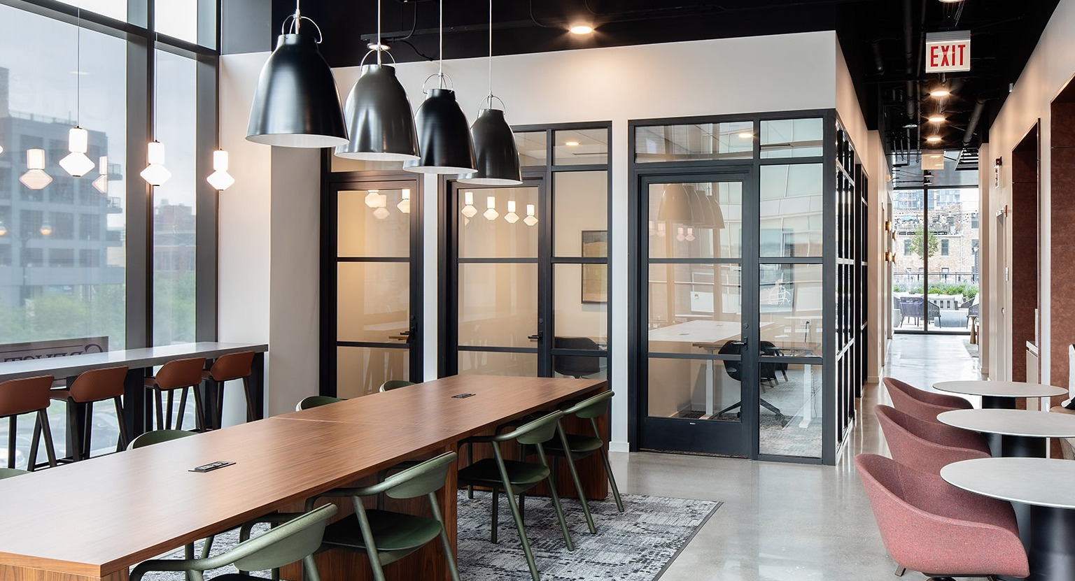 Modern coworking space with a large communal table, private offices, and comfortable booth seating at One Six Six