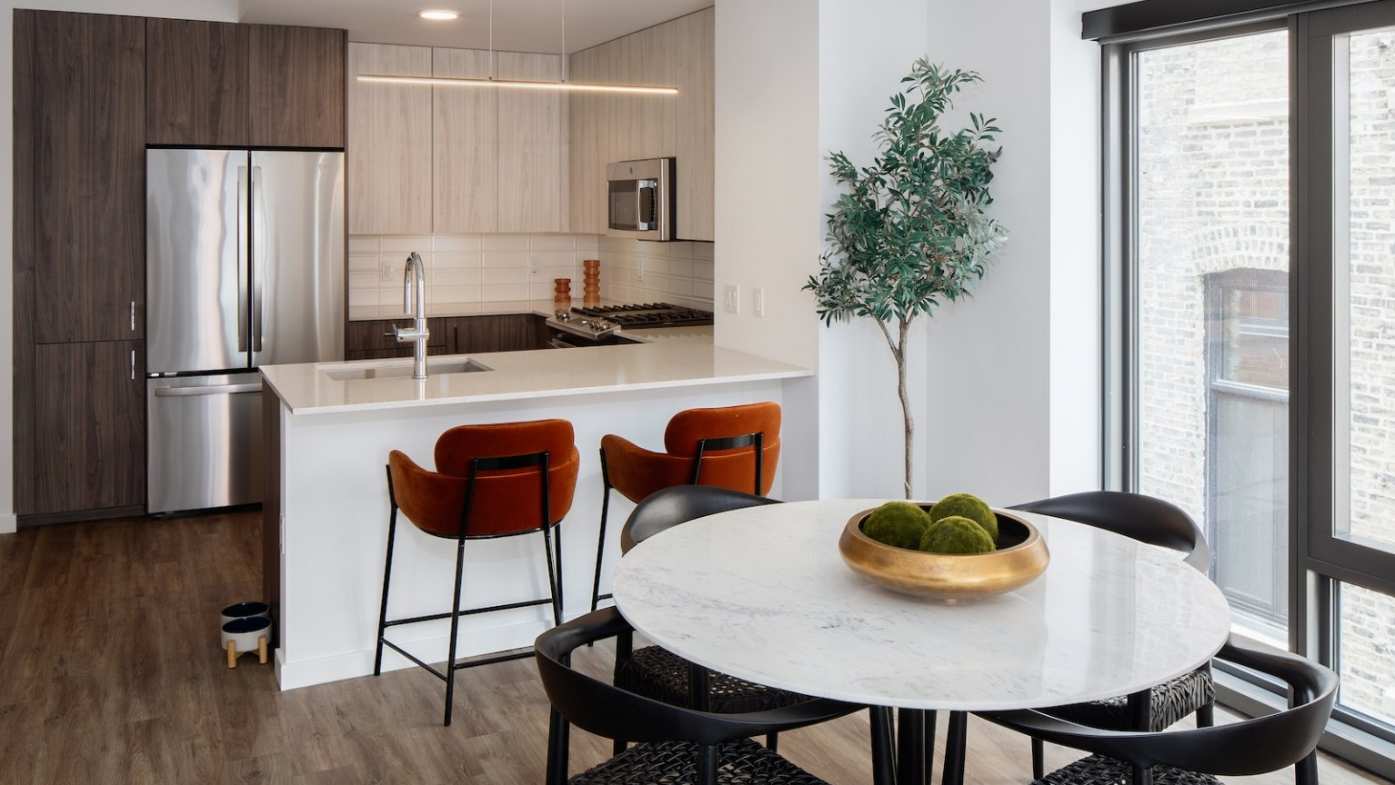Contemporary kitchen with a dining area, bar seating, stainless steel appliances, and a tall plant at One Six Six