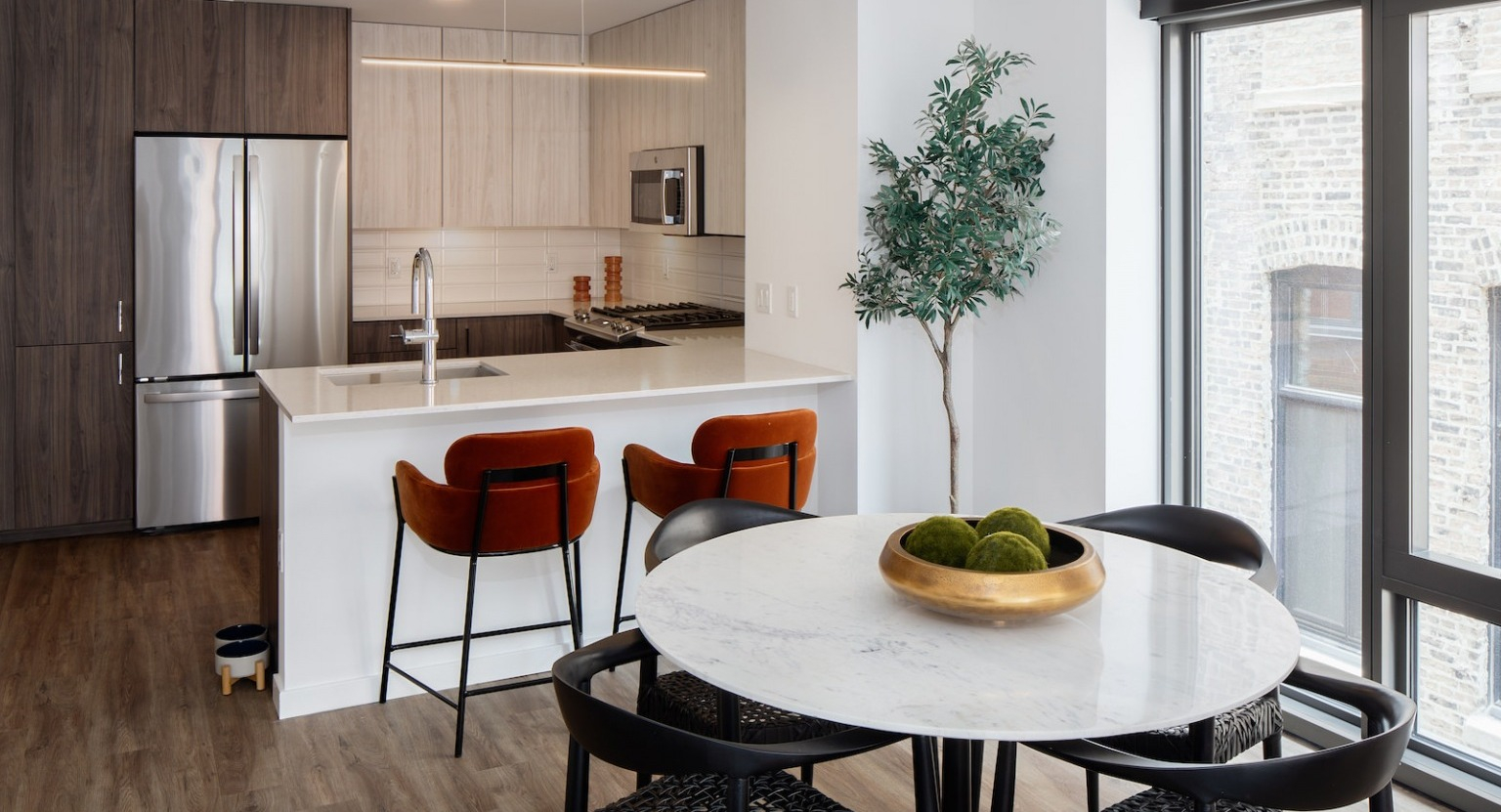 Contemporary kitchen with a dining area, bar seating, stainless steel appliances, and a tall plant at One Six Six