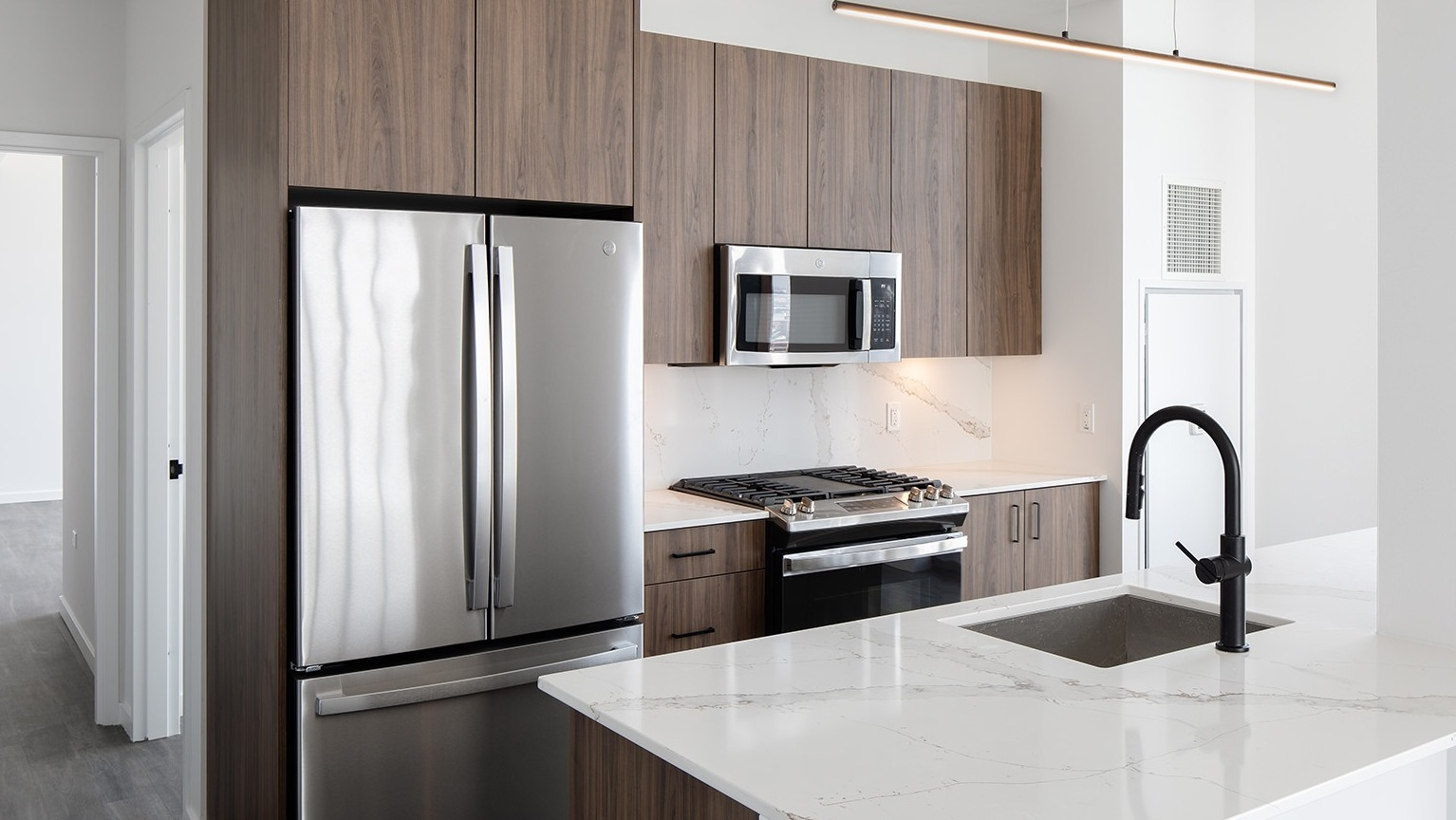 Modern kitchen with wood-look cabinetry, stainless steel appliances, a large island, and a sleek faucet at One Six Six