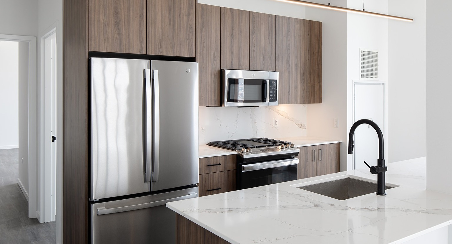 Modern kitchen with wood-look cabinetry, stainless steel appliances, a large island, and a sleek faucet at One Six Six