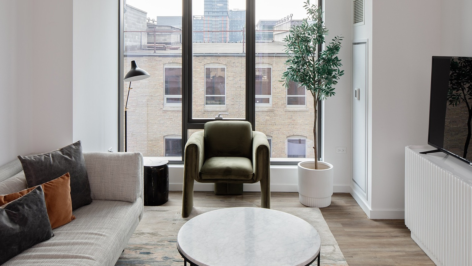 Inviting living room with comfortable seating, a television, and large windows offering urban views at One Six Six