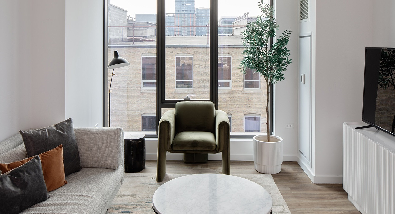 Inviting living room with comfortable seating, a television, and large windows offering urban views at One Six Six