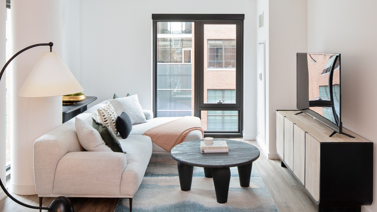 Modern and cozy living room with a large sofa, accent rug, stylish coffee table, and large window at One Six Six